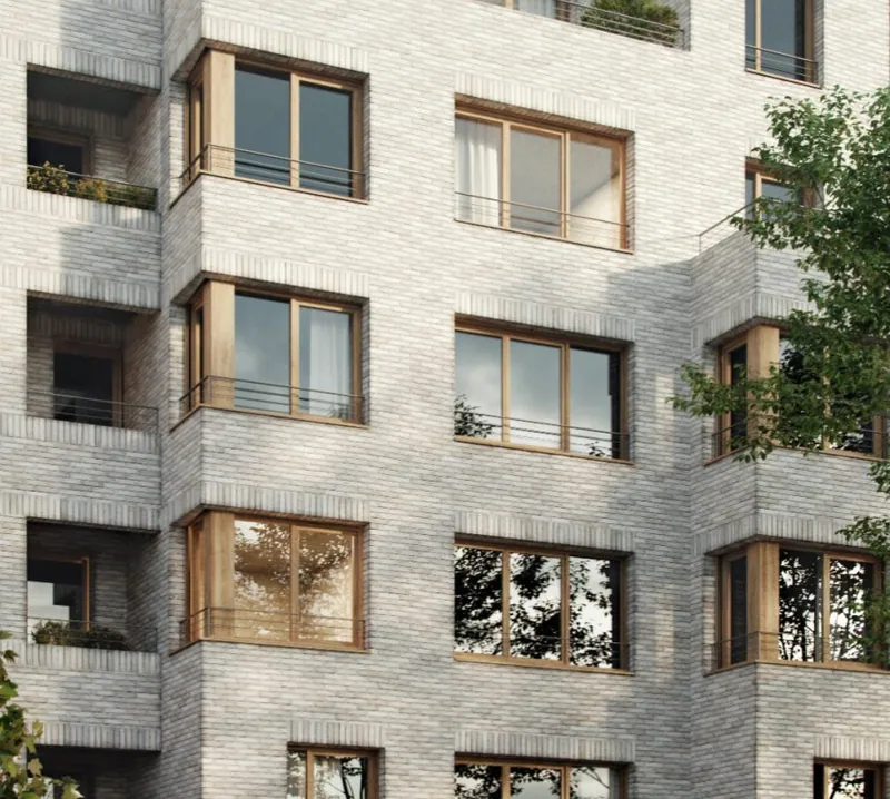 Détail de façade : brique claire appareillée, encadrements et menuiseries en bois, garde-corps métalliques fins, loggias plantées.