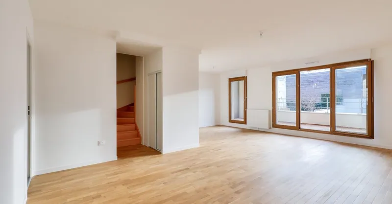 Séjour livré d'un duplex : parquet chêne, escalier bois, grandes menuiseries bois ouvrant sur une terrasse.