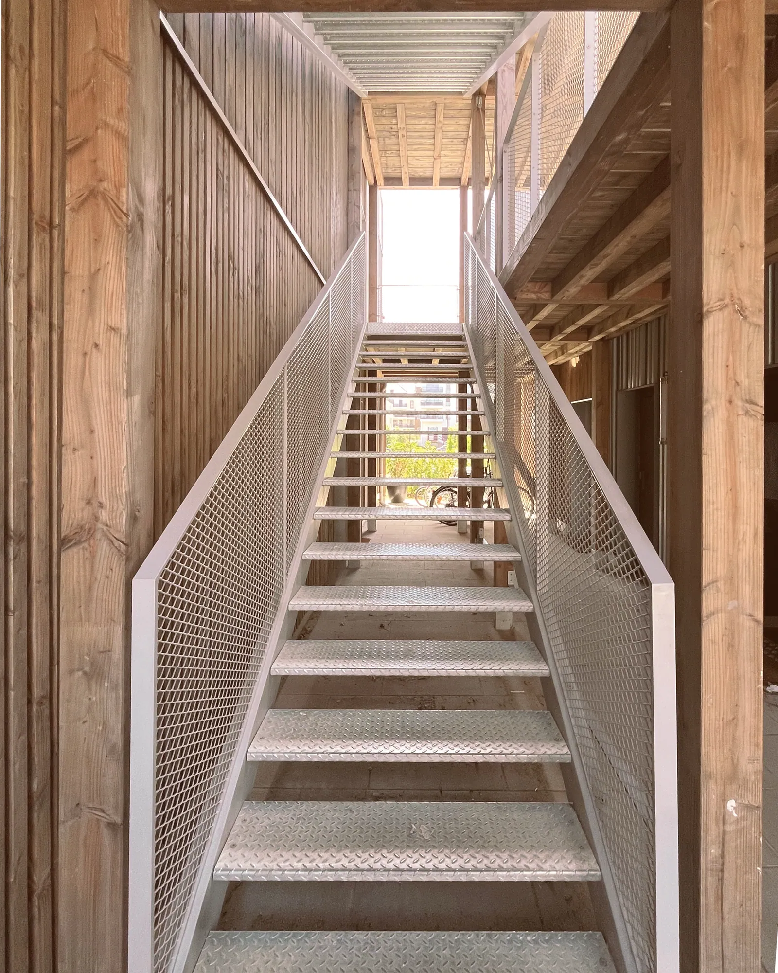 Escalier métallique en maille déployée dans un passage bardé de bois, à Belle-Île-en-Marne.